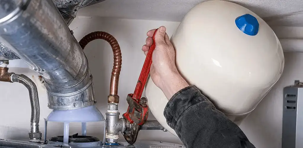 Water heater repair technician tightening plumbing connections near a tank unit in Orange, CA